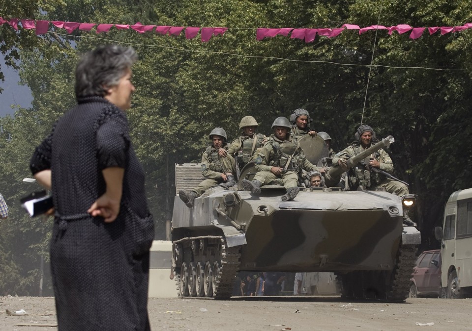 Uma mulher observa tanque russo passando pela cidade de Dzhava | Reuters