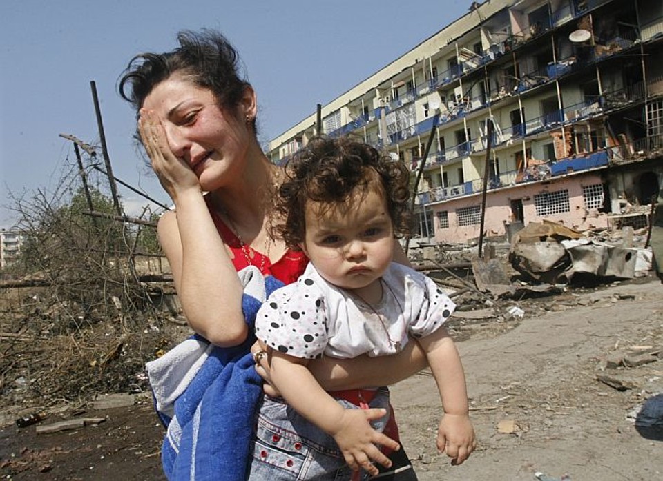 Mulher georgiana chora, com a criança no colo, em frente ao bloco de apartamentos civis bombardeados por tropas russas | David Mdzinarishvil/Reuters