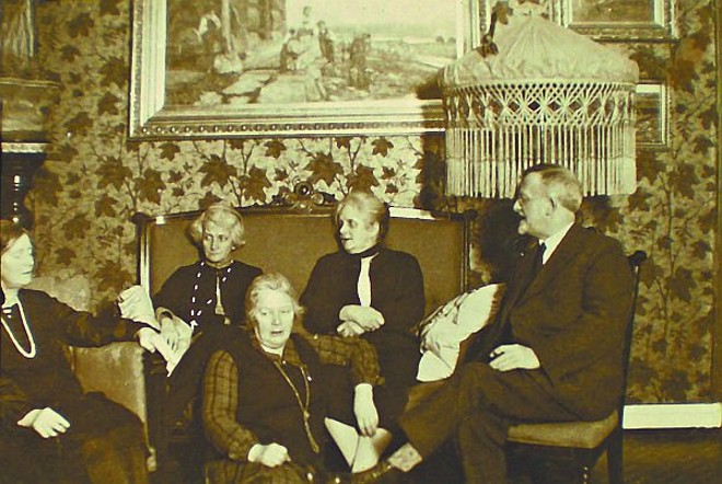 Andersen com irmãs e familiares durante sua visita à Noruega, em 1928. Ao fundo, um quadro, também com temática folk, pintado por ele nos anos 1890 |