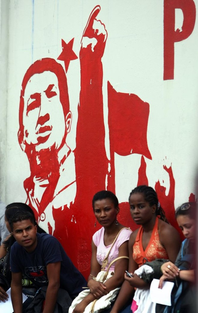 Moradores de Caracas esperam ônibus em frente de painel com propaganda chavista: projeto de socialismo do século 21 será avaliado nas urnas | Thomas Coex/AFP
