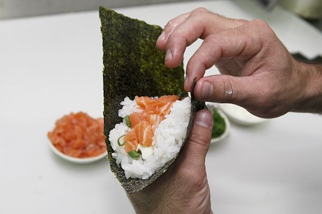 4 - Enrole pegando a ponta do canto inferior esquerdo com os dedos indicador e polegar e leve até a extremidade superior esquerda. Vá enrolando, com firmeza, com a mão direita até formar um cone | 