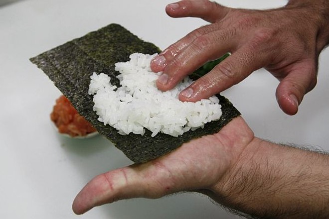 2 - Sobre o lado mais fosco da alga, na parte inferior, espalhe o arroz japonês Gohan com o auxílio de uma colher até formar uma camada de mais ou menos 0,5 centímetro | 