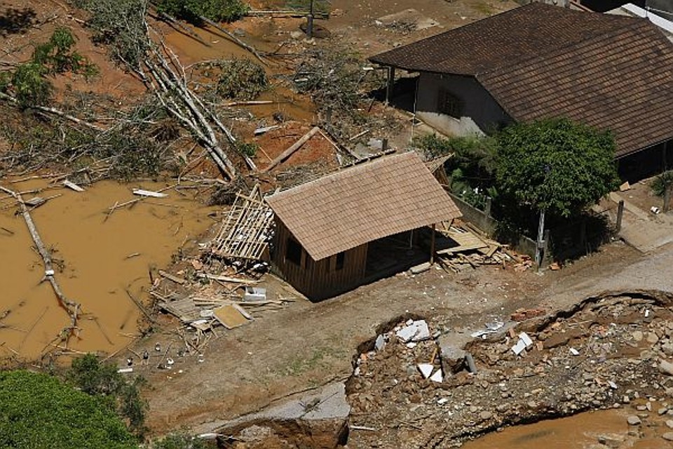 A rua que virou rio - Na frente da casa da família Sperber passava um riacho no qual, dependendo do dia, podia-se pular nas pedras sem molhar o pé. Desde sábado o riachinho estava enchendo de uma maneira nunca vista, por causa da chuva forte. Até fomos deitar porque nunca nos preocupamos com o rio, conta a mãe Ana Maria Sperber. A chuva ficou mais forte e era um tormento ouvir o barulho das pedras. O filho que morava na casa ao lado acordou à meia-noite e viu que a garagem da casa dos pais estava alagada. A estrada tinha virado rio. Mãe, pai, dois filhos, nora grávida de três meses e casal de primos fugiam da chuva. Foram resgatados pelo helicóptero na quarta-feira |