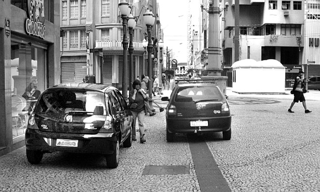 Automóveis estacionados no calçadão. |