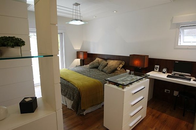 Ao lado da cama de casal fica um móvel de apoio com uma pequena vitrine para os objetos de Cléris, com a função de uma penteadeira |