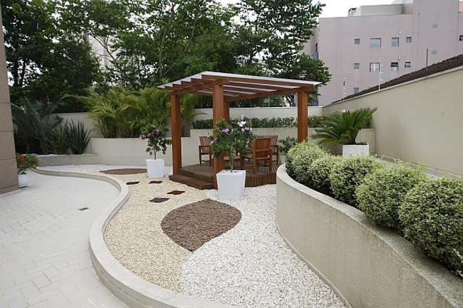 Vasos sob pedriscos em muretas de vários níveis e um gazebo de madeira com cobertura de policarbonato compõem o jardim do apartamento |