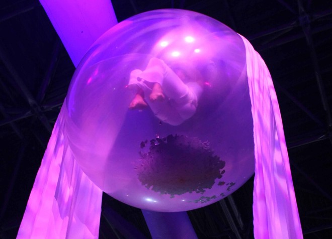 Durante a festa, suspensa no ar, bailarina realiza performance dentro de bolha em cima do público | 