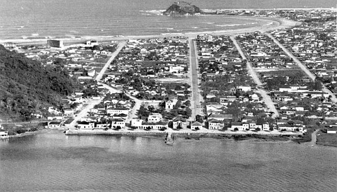 O outro local procurado pelo curitibano, principalmente nas férias escolares, é a cidade balneária de Guaratuba. A fotografia aérea feita, em 1962, mostra a cidade vista da baía em direção à praia. Parte das casas que aparecem em primeiro plano foi engolida por afundamento que o local sofreu em 1968, desaparecendo sob as águas da baía | 