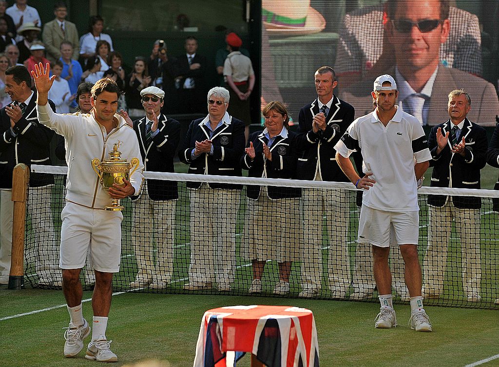 Com Pete Sampras no telão e o vice-campeão Andy Roddick ao lado, Roger Federer recebe o seu sexto troféu no All England Club | Carl de Souza/AFP
