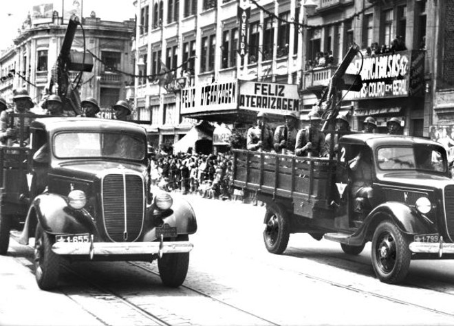 Desfile militar na Avenida. O 5º Regimento de Aviação desfila com viaturas providas de metralhadoras antiaéreas, em 1938. No Cine Avenida, o filme anunciado: Feliz Aterrissagem | 