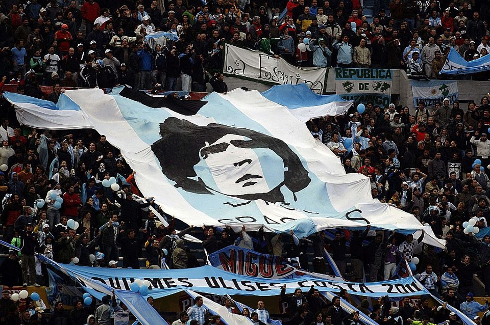 Um bandeirão no meio da torcida argentina agradece a Deus pela existência de Diego Maradona: técnico não tem emprego garantido até o Mundial | Enrique Marcarian/Reuters