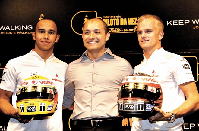 O engenheiro curitibano Ronald Szafirski entre os pilotos Lewis Hamilton e Heikki Kovalainen. O nome dele está inscrito na parte superior frontal dos dois capacetes |