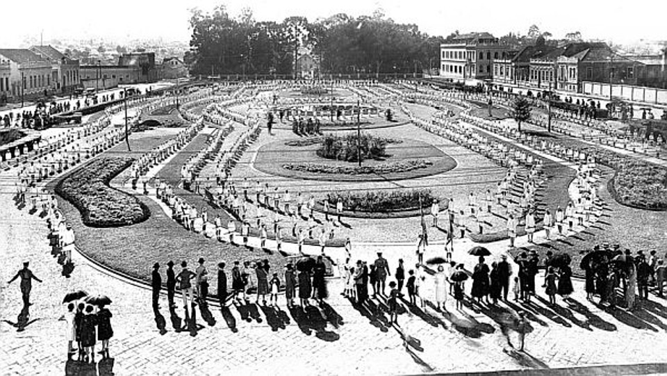 Praça Santos Andrade, em 1927. A fotografia foi feita de uma das janelas da Universidade, em direção ao bosque que existia na então chácara da família de Ventura de Almeida Torres espaço hoje ocupado pelo Teatro Guaíra. A imagem foi gravada em razão de estar ocorrendo uma comemoração cívica, com a participação de alunos de escolas primárias de Curitiba |