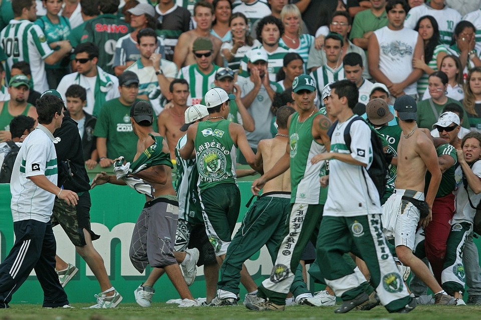 Enquanto o massagista do Fluminense (à direita, de calça de vermelho) era espancado, Reimackler Graboski (de boné e regata), vice da Império Alviverde, caminhava tranquilamente pelo gramado: dos torcedores que aparecem na imagem, sete claramente usam adereços da organizada | Fotos: Heuler Andrey/Agência Estado