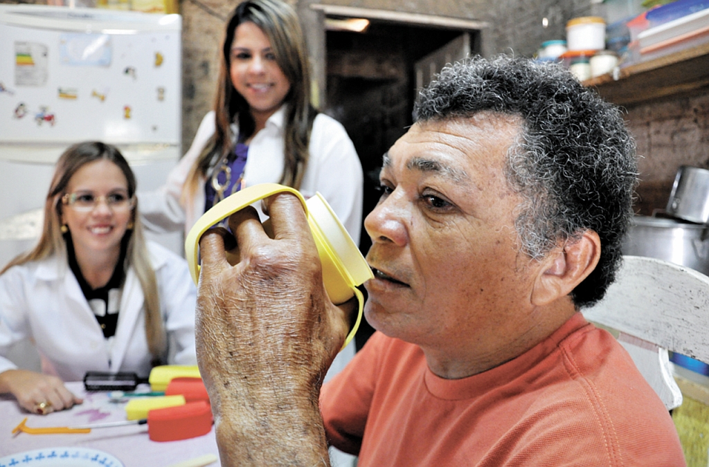 Paciente de Natal usa adaptação de EVA para copo sob a orientação das terapeutas ocupacionais Lorena Lopes e Lorena Pimentel (em pé) | Eduardo Maria/DND A. Press