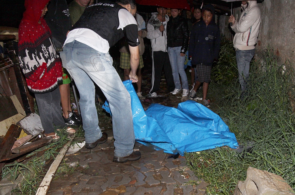 Perito analisa corpo de uma das vítimas no Jardim Arroio, no Barreirinha: assassinato ocorrido há duas semanas na mesma região teria motivado vingança, que deixou seis mortos | Giuliano Gomes/ Gazeta do Povo