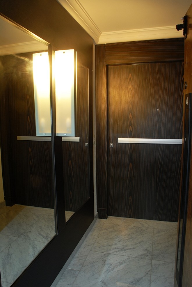 Porta de tonalidade escura, da arquiteta Vivian Calissi, ganha claridade com a luminária e com o espelho na parede lateral |