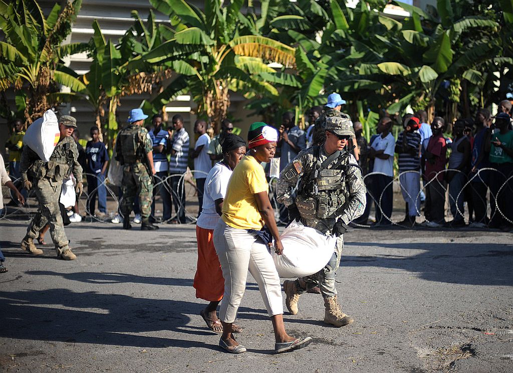 Soldado ajuda haitianas a transportar alimentos enviados por outros países: segurança para evitar desvio de doações | Roberto Schmidt/AFP