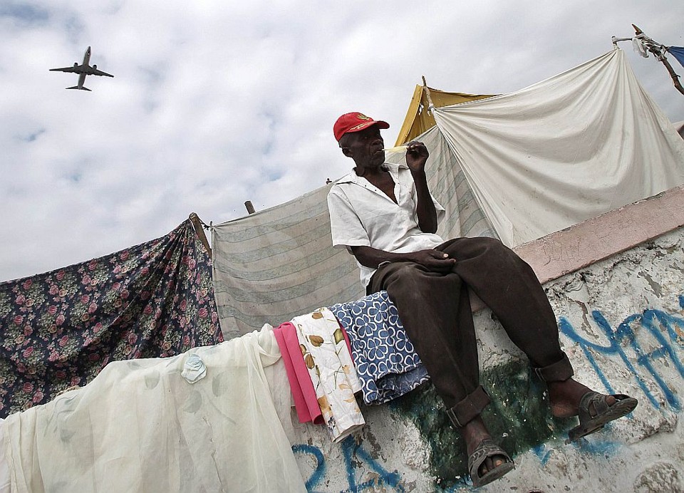 Primeiro voo comercial para o Haiti após a tragédia passa atrás de haitiano em campo de desabrigados pelo terremoto | Reuters