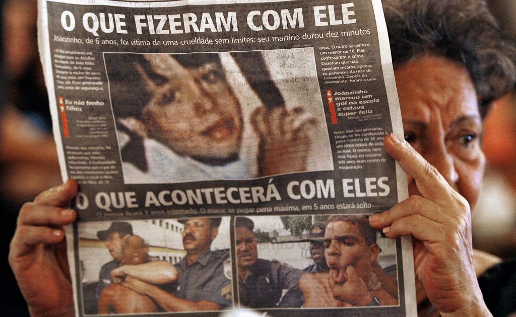 Mulher mostra fotos de João Hélio e dos acusados durante a missa de sétimo dia pela morte do garoto, em 2007 | Vanderlei Almeida / AFP