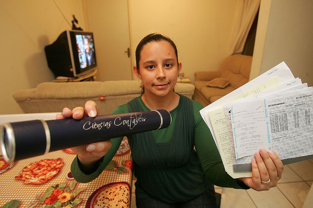 A contabilista Daiane Luz dos Santos, com o canudo e as faturas do Fies: Sem o financiamento, eu realmente não teria conseguido terminar o curso | Daniel Castellano/ Gazeta do Povo