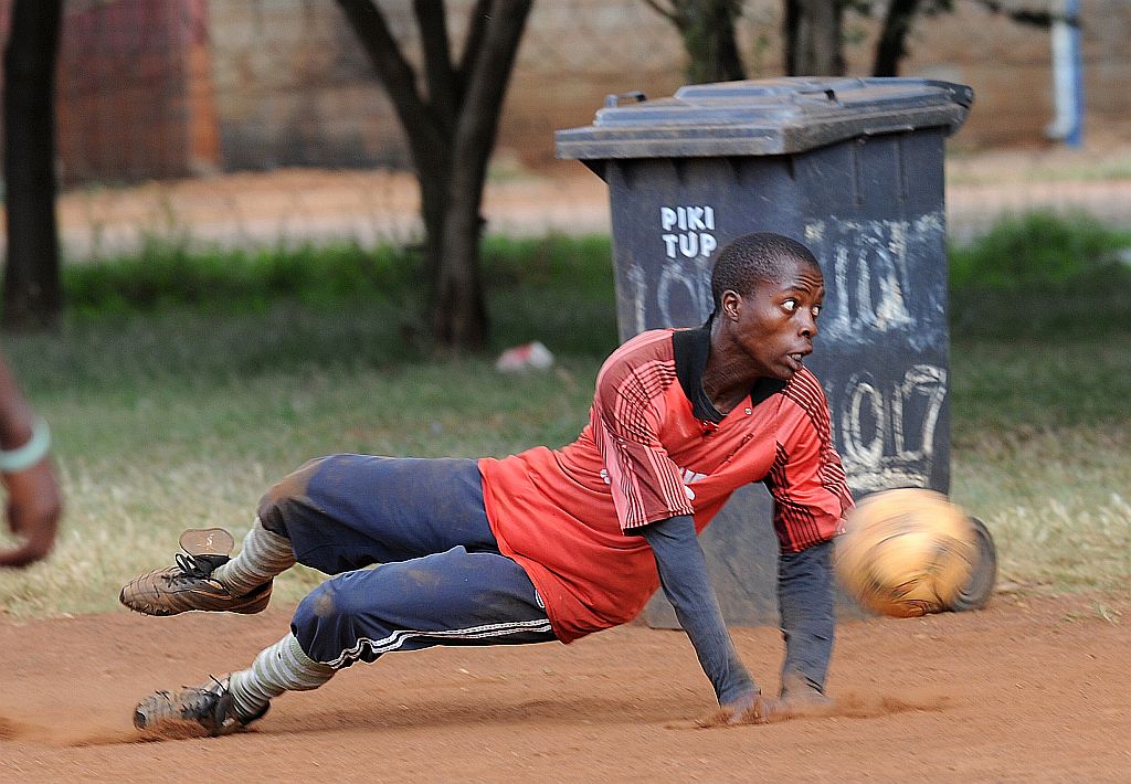 Com uma bola velha e latões de lixo como trave, o terreno de chão batido vira campo de pelada no Soweto, o famoso bairro negro de Johannesburgo | Alexander Joe/ AF