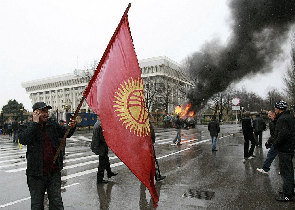 Manifestante fala ao celular enquanto carrega bandeira do Quirguistão em frente ao palácio presidencial | Reuters