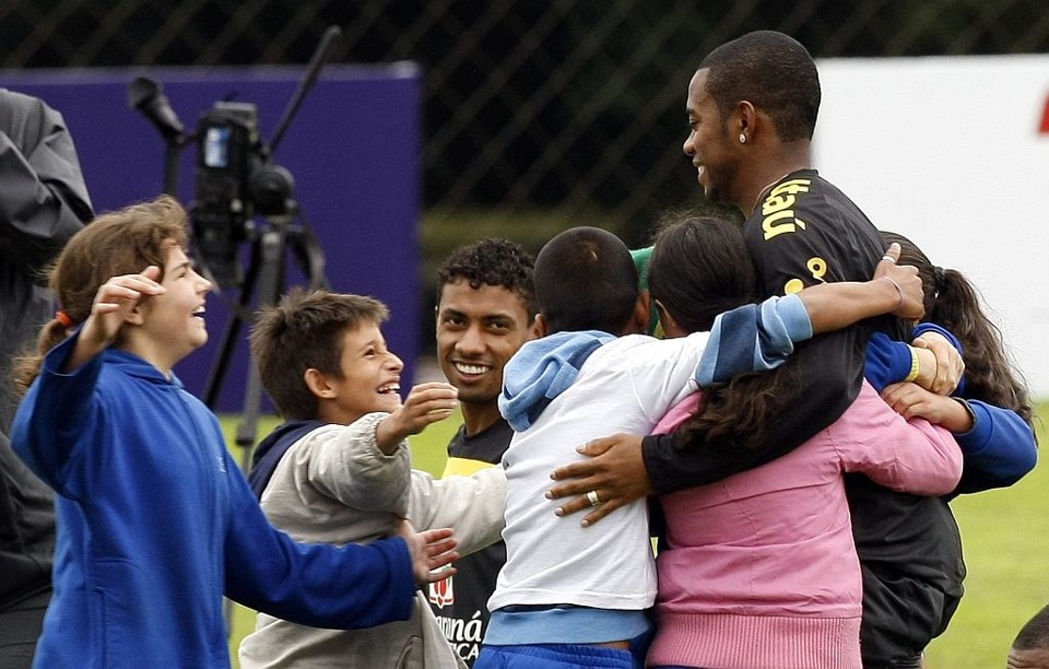 Momento de emoção - Após um início de clausura no Centro de Treinamentos do Caju, do Atlético, os jogadores e integrantes da comissão técnica da seleção brasileira abriram as portas do treino de ontem para visitantes especiais. Meninos e meninas com problemas auditivos da Escola Central Tarumã, de Curitiba, foram autorizados a entrar no campo e levaram o carinho e o apoio ao time de Dunga. As crianças nem acreditaram. Cercavam e abraçavam os seus ídolos, que também ficaram visivelmente emocionados. Foi muito bonito o que aconteceu. É gratificante saber que podemos levar alegria a essas crianças, foi um momento que valeu a pena vivenciar, disse o técnico Dunga, um dos mais assediados pelas crianças, ao site oficial da CBF.  Entre os jogadores, Robinho  na foto observado por Kléberson  foi o mais procurado pelos pequenos visitantes | Reuters
