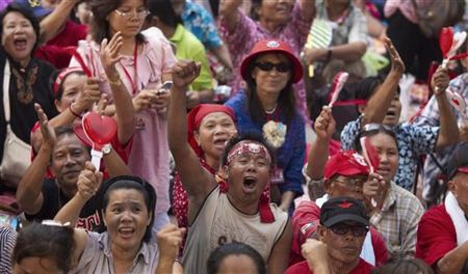 Camisas vermelhas contrários ao governo acampados no distrito comercial de Bangcoc se manifestam enquanto líderes fazem discurso no palco. Os manifestantes criticaram a convocação de eleições para novembro. | REUTERS/Adrees Latif