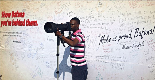Um fotógrafo trabalha em frente de um cartaz com as assinaturas de torcedores sul-africanos, desejando que a sua equipe vá bem na Copa do Mundo | 