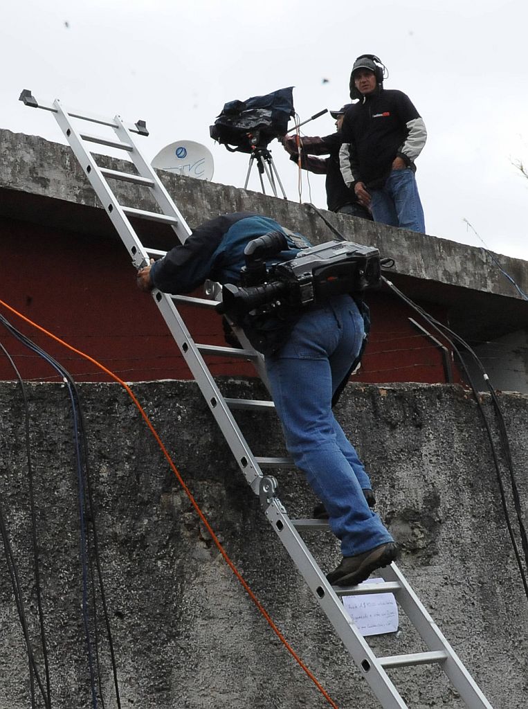 Cinegrafista escala parede para conseguir um bom ângulo para cobrir a chegada da seleção. Precariedade marca o trabalho | Vanderlei Almeida/ AFP