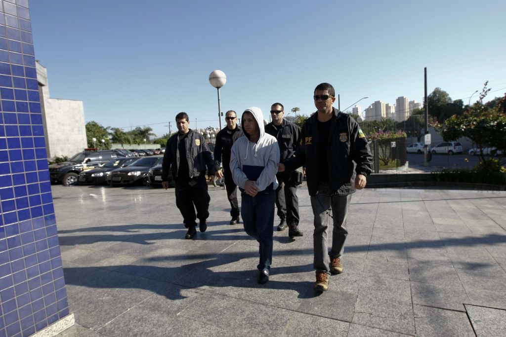 Policiais federais conduzem um dos 12 suspeitos detidos na operação: fraudes beneficiaram pelo menos 120 pessoas | Apu Gomes/Folhapress