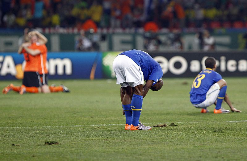 O lateral-direito brasileiro Maicon arruma a meia, ainda sob o choque da eliminação da Copa do Mundo, enquanto Daniel Alves, agachado, parece tentar entender o que aconteceu em Port Elizabeth. Ao fundo, holandeses se abraçam após o triunfo | Valterci Santos/Gazeta do Povo enviado especial