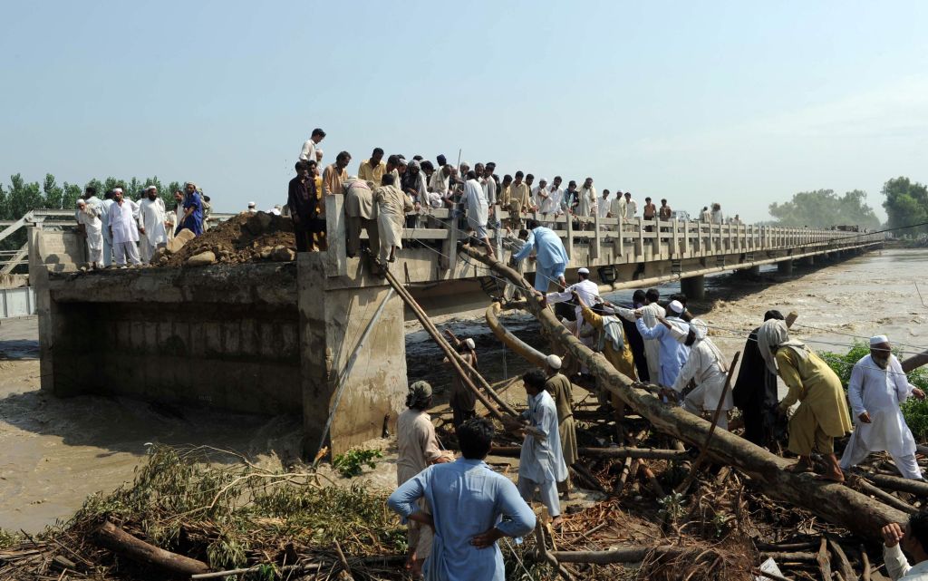 Paquistaneses usam cordas e madeira para escalar uma ponte danificada pelas enchentes em Charsada: cerca de 27 mil pessoas estão isoladas no país | A. Majeed/AFP