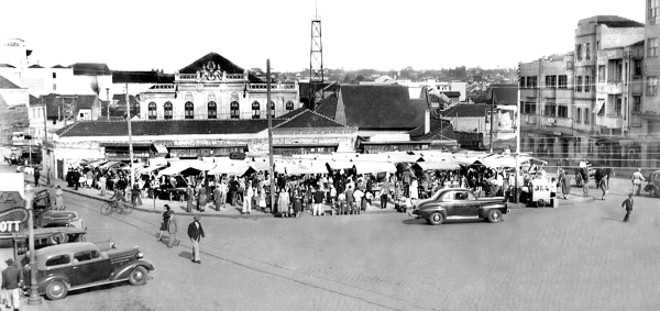 PRAÇA TIRADENTES O logradouro mais importante de Curitiba, o Coração da Cidade. Ponto central de onde se desenvolveu a urbe. Largo da antiga Matriz, da Cadeia Pública e da Câmara Municipal. Concentrou o comércio da cidade em seu núcleo e arredores. Sem dúvida alguma, a centenária Catedral é o seu edifício mais importante. Na fotografia, aparece uma feira livre instalada no terreno baldio do antigo Banco do Brasil, onde está a sede do atual. Ao fundo, vemos a fachada do Theatro Guayra e a torre do Corpo de Bombeiros. A foto é de 1946 | 