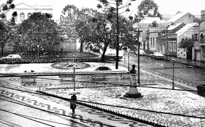 PRAÇA GARIBALDI A fotografia é do dia 17 de julho de 1975, quando Curitiba foi brindada com uma bela e gelada nevada. Na praça existe a Igreja do Rosário, a nova, construída no final da década de 1930, substituindo a antiga, em estilo colonial, construída pelos escravos, ficando conhecida como Igreja dos Pretos. Após a inauguração do Cemitério Municipal, o templo passou a ser conhecido como a Igreja dos Defuntos, quando ali se faziam a encomendação dos mortos. Imponente é a construção da Sociedade Garibaldi, obra erigida pela sociedade italiana de Curitiba | 
