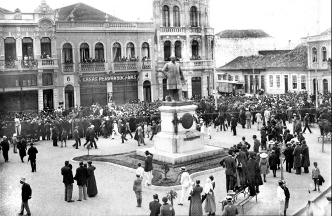 PRAÇA GENEROSO MARQUES Antiga Praça Municipal ou do Mercado. Ali, no final do século dezenove e princípio do vinte, concentrava-se o grande comércio curitibano aonde os colonos vinham com suas enormes carroças de oito cavalos trazendo mercadorias produzidas no interior e voltavam com elas repletas de víveres, ferramentas e tecidos. Em 1915, o Mercado Municipal estava desativado e em seu lugar surgia o prédio da prefeitura. Foi naquele ano que se deu a inauguração do monumento ao Barão do Rio Branco, cuja iniciativa popular foi originada por João Gualberto, em 1912, pouco antes de falecer na primeira batalha da Campanha do Contestado. Foto de 1915 | 
