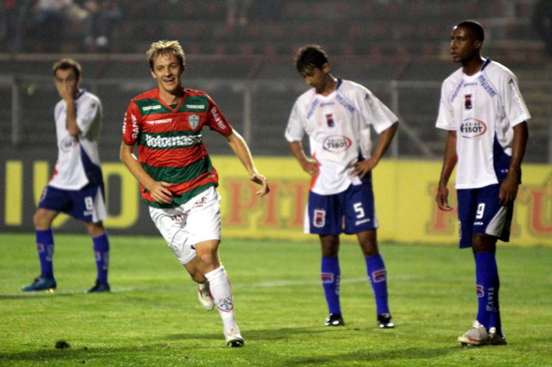 Ademir Sopa corre para comemorar um dos gols da Lusa, enquanto o zagueiro Alessandro Lopes baixa a cabeça ao fundo | Roberto Vazquez / Futura Press