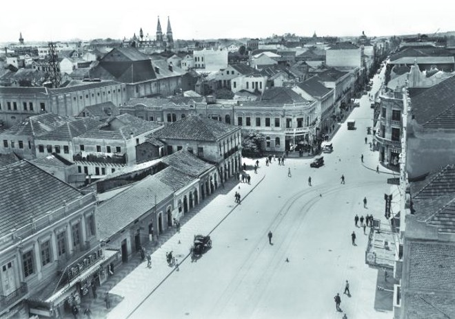 A fotografia é da Avenida Luiz Xavier e Rua Quinze de Novembro. Essa última ainda sendo mais estreita que a avenida. À esquerda, temos a torre dos Bombeiros; o telhado do Theatro Guayra se sobressai, e a Catedral aparece imponente na cidade rasa. |