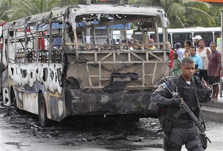 Policial passa em frente a ônibus queimado no bairro de Vicente de Carvalho no Rio de Janeiro | Reuters