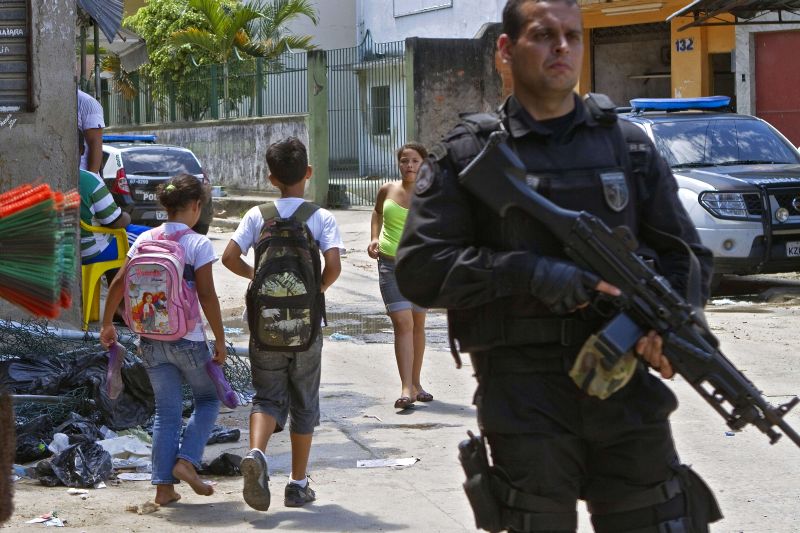 Policial vigia a região do Morro do Alemão enquanto as crianças seguem para a aula | Jefferson Bernardes/AFP