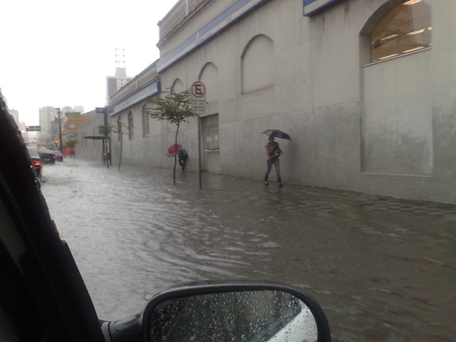 Pedestres tentam escapar da água que ficou acumulada na calçada e asfalto da Avenida Visconde de Guarapuava |