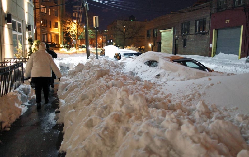 Em Nova Jersey, nos EUA, pedestres usam canto de calçada em rua com carros cobertos por neve | Reuters