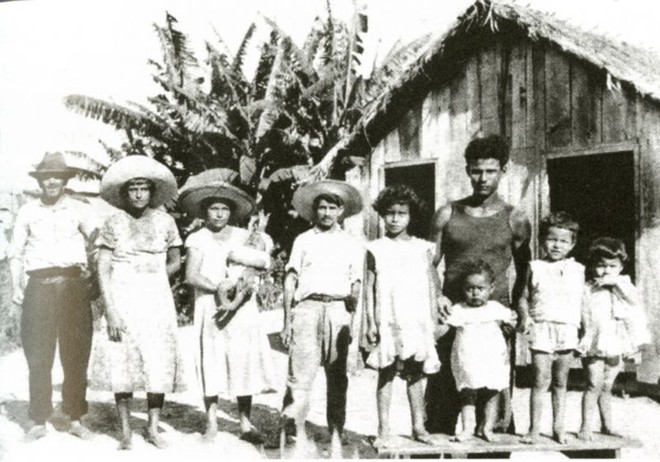 Caboclos em frente a uma casa típica feita com tábuas e folha de palmeira |