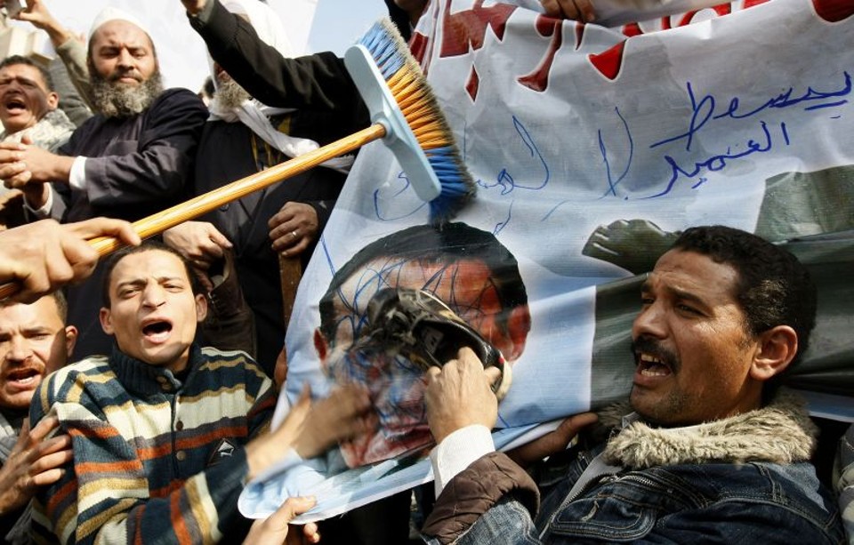 Manifestantes egípcios usam um sapato e uma vassoura para bater na foto do Presidente Hosni Mubarak, durante um protesto na praça Tahrir, no Cairo, em 30 de janeiro de 2011 | MOHAMMED ABED/AFP