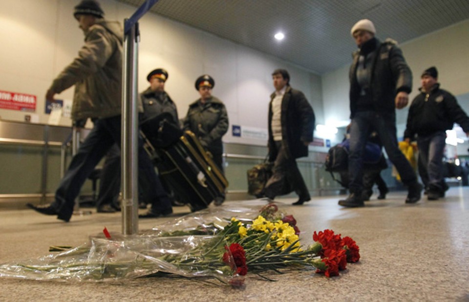 Flores são deixadas nesta terça-feira (25) em homenagem aos mortos pelo atentado da véspera, em saguão no aeroporto russo de Domodedovo; ao fundo, policiais montam guarda | Reuters