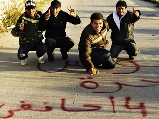Imigrantes tunisianos que chegaram ilegalmente a Lampedusa posam para foto nesta terça-feira (15). A mensagem escrita no chão celebra, em árabe, a democratização do país | Reuters