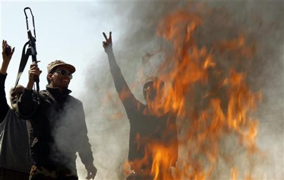 Rebeldes comemoram diante do fogo ateado em roupas de soldados leais a Muammar Kadafi, entre Benghazi e Ajdabiyah, na Líbia | REUTERS/Goran Tomasevic