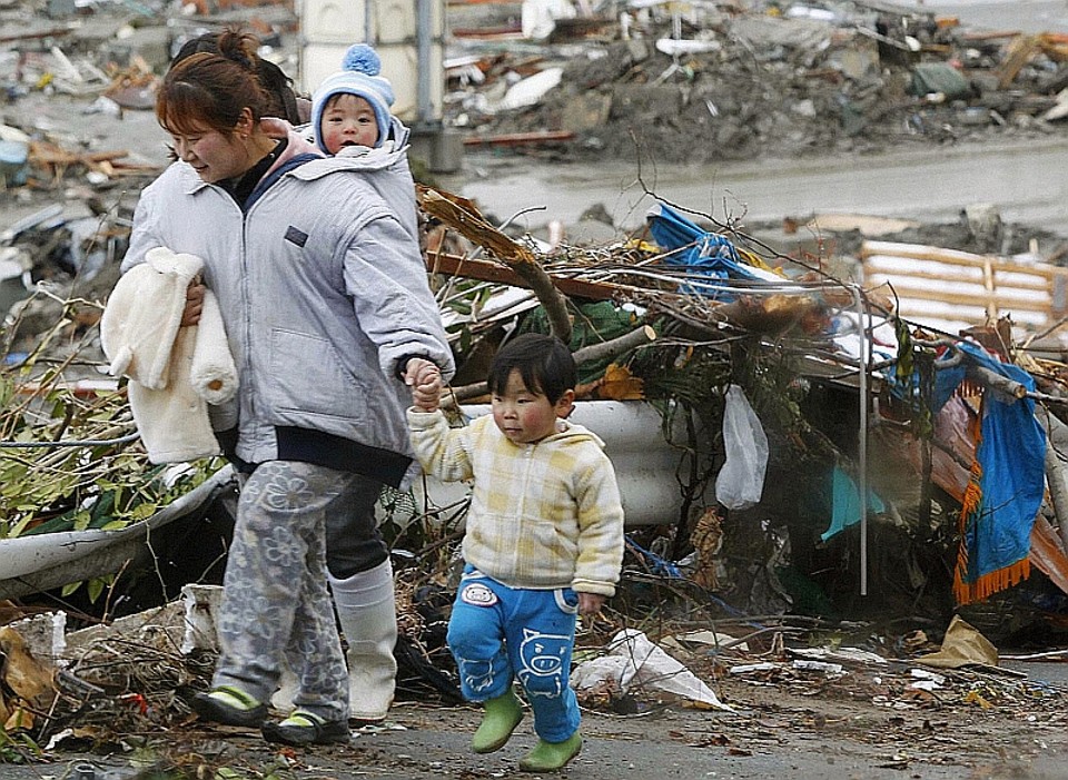 Família passa pelos escombros na cidade de Minamisanriku, no Japão | REUTERS/Kyodo