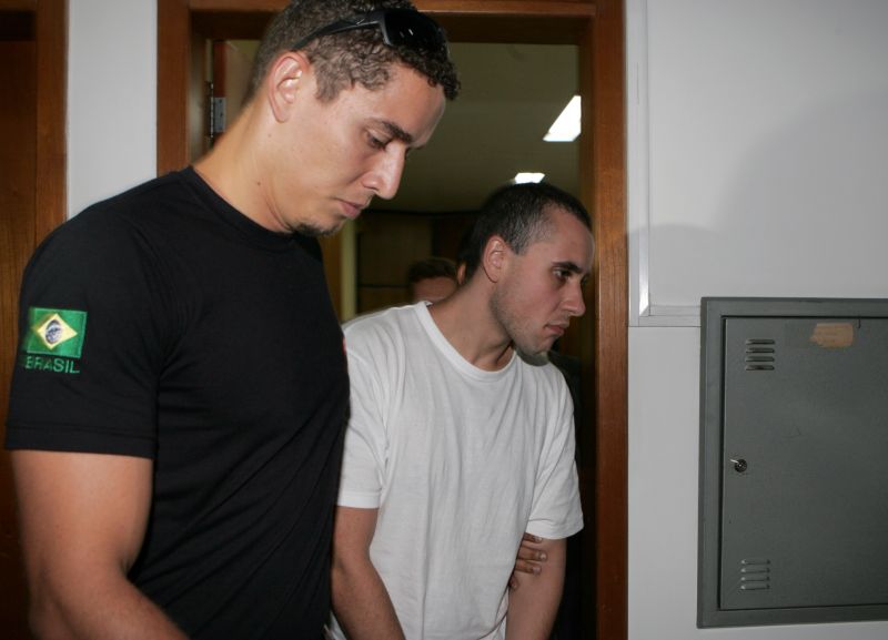 Cadu (à direita) é escoltado por policial na audiência em Foz: defesa tenta provar que ele é inimputável | Christian Rizzi / Gazeta do Povo